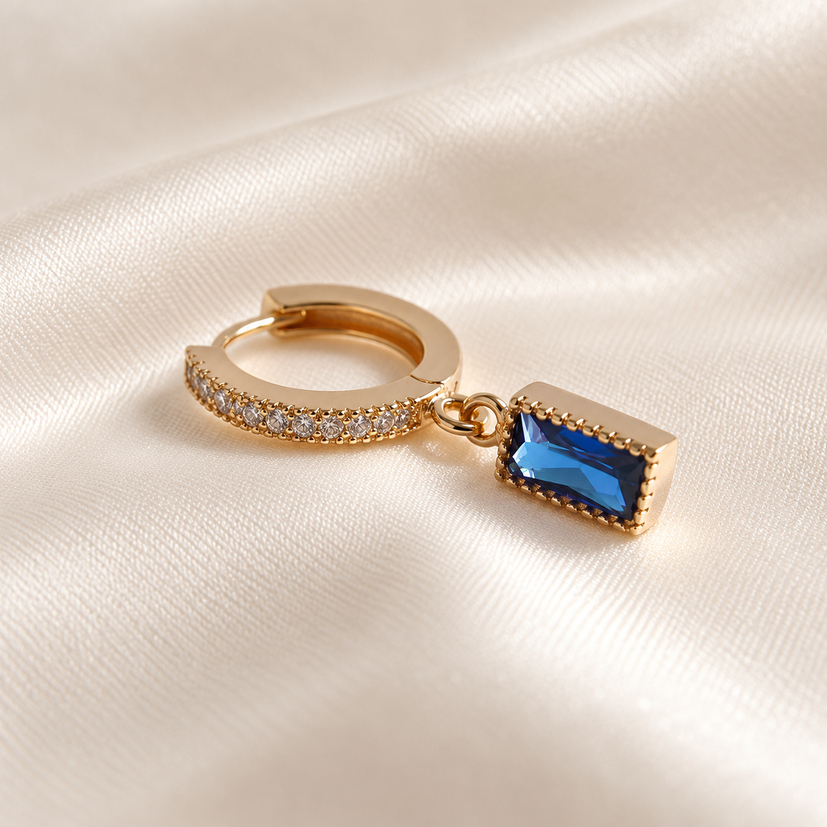 Digital product visualisation: Champagne Gold single blue CZ drop earring on ivory silk; macro view