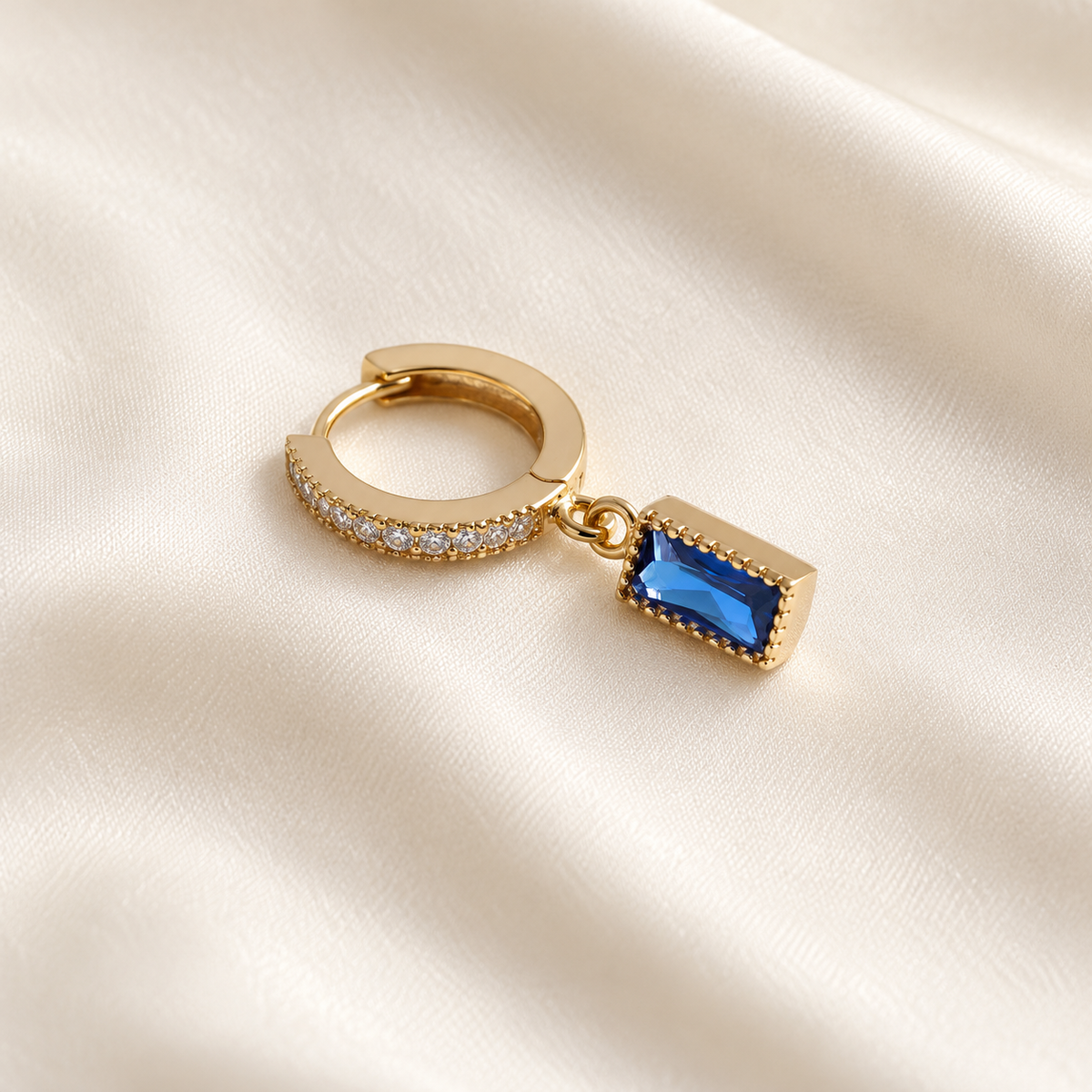 Digital product visualisation: Champagne Gold single blue CZ drop earring on ivory silk; overhead view