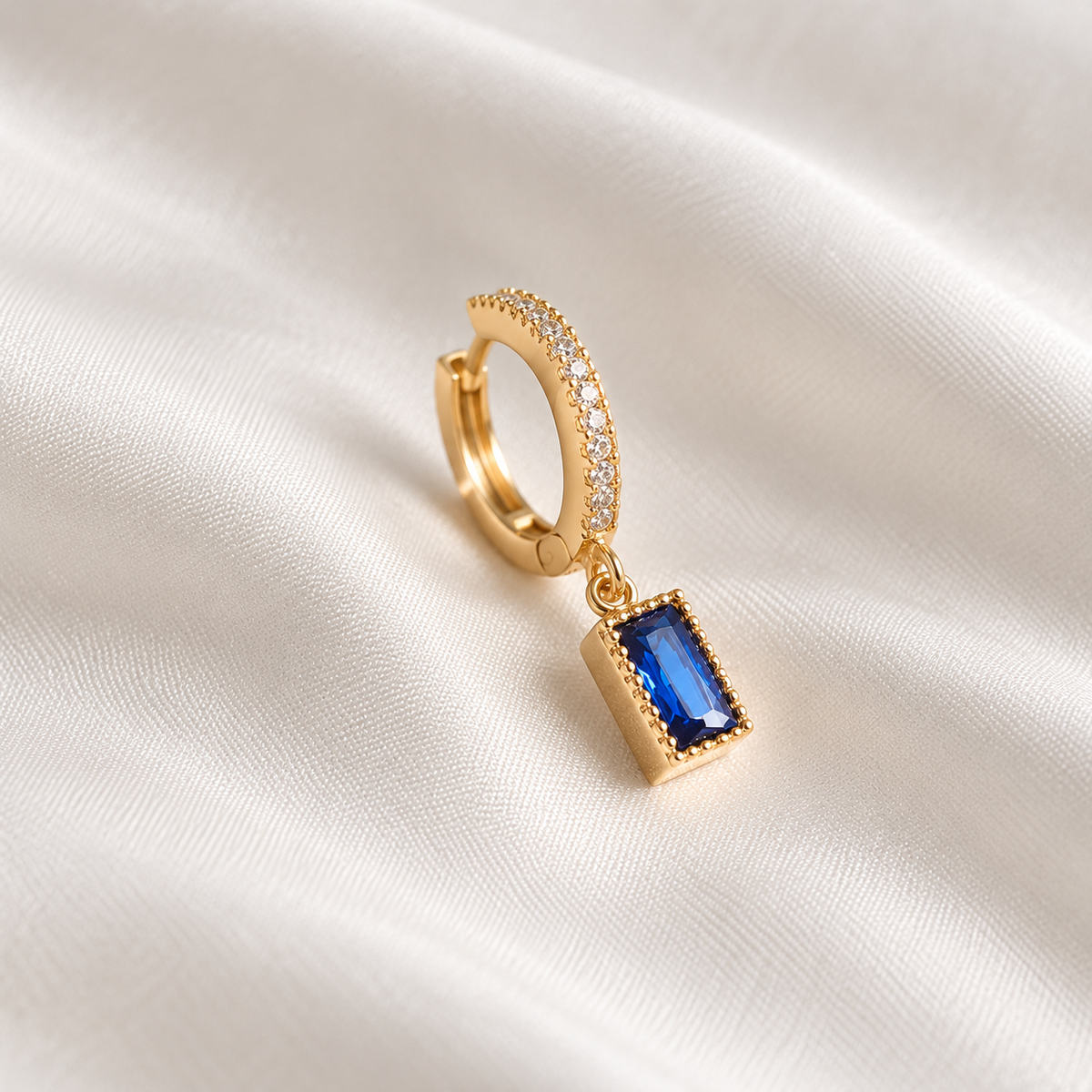 Digital product visualisation: Champagne Gold single blue CZ drop earring on ivory silk; side view