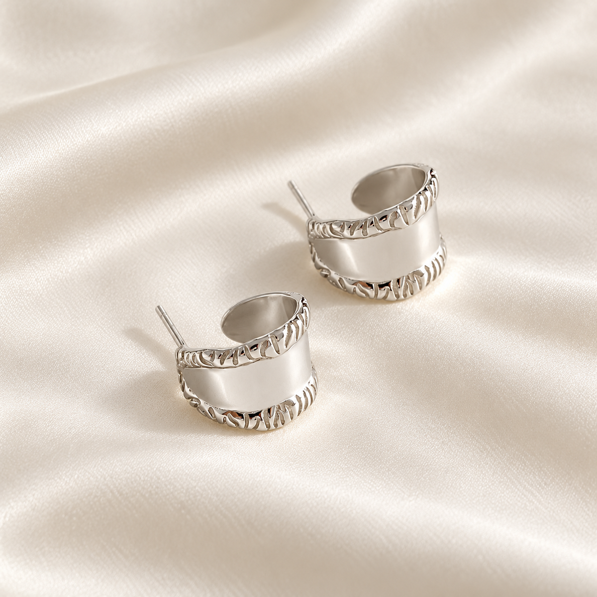 Digital product visualisation: silver carved wide stud earrings on ivory silk; overhead view