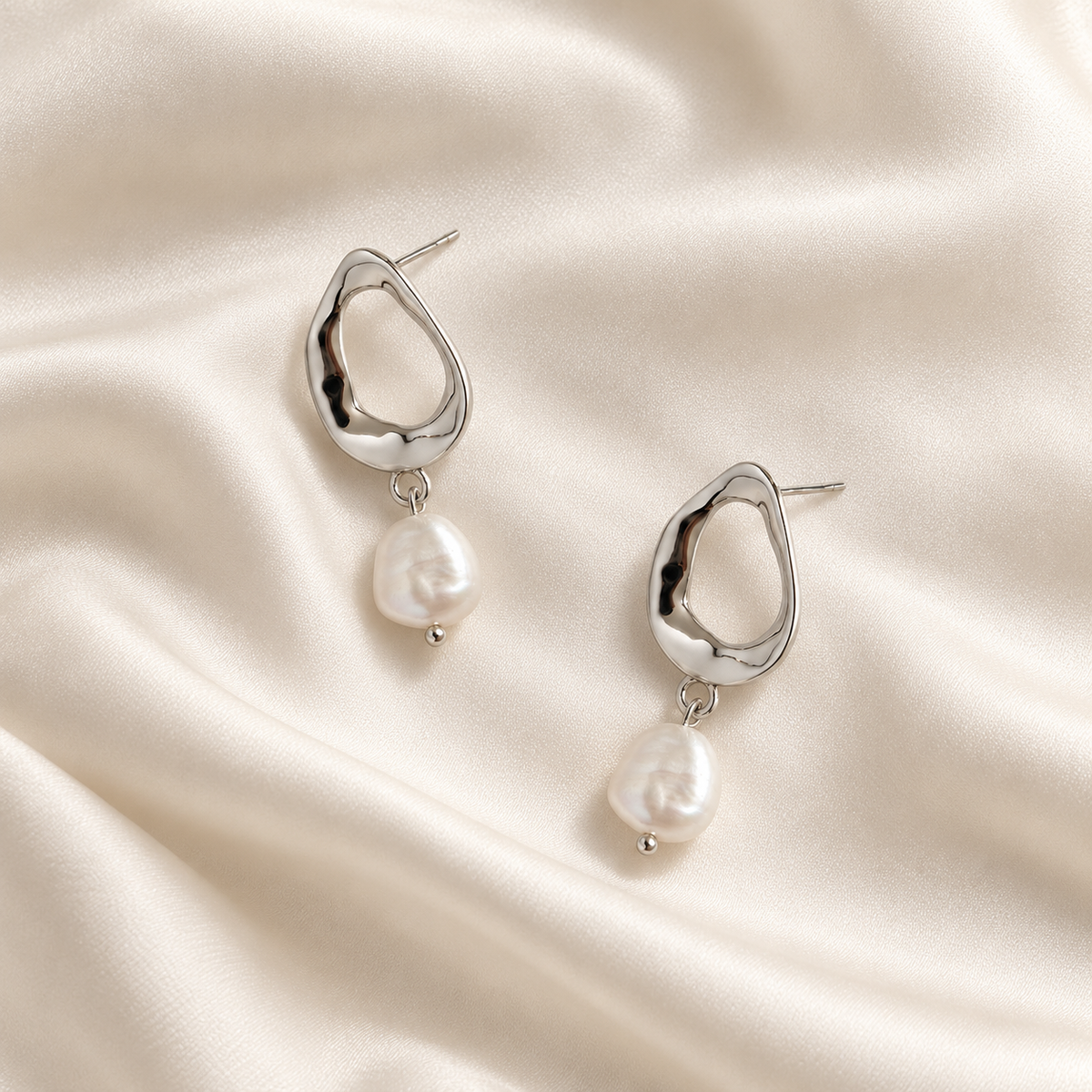 Digital product visualisation of pearl drop earrings in silver finish on ivory silk, overhead view