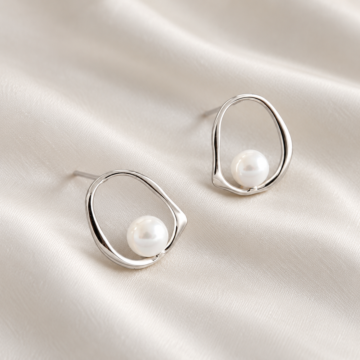Digital product visualisation: silver shell pearl stud earrings on ivory silk; overhead view